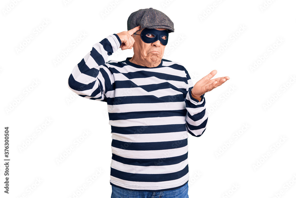 Senior handsome man wearing burglar mask and t-shirt confused and annoyed with open palm showing copy space and pointing finger to forehead. think about it. Senior handsome man wearing burglar mask and t-shirt confused and annoyed with open palm showing copy space and pointing finger to forehead. think about it.