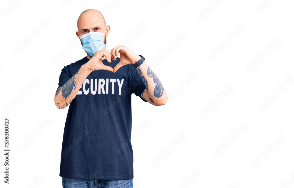 Young handsome man wearing security t shirt and medical mask smiling in love showing heart symbol and shape with hands. romantic concept. Young handsome man wearing security t shirt and medical mask smiling in love showing heart symbol and shape with hands. romantic concept.