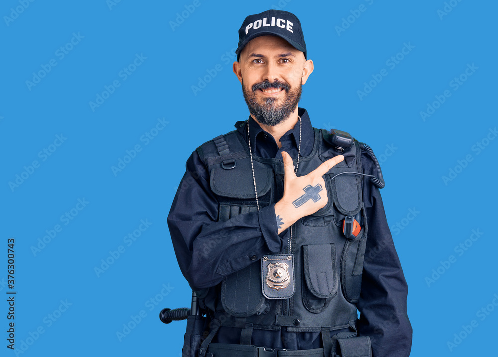 Young handsome man wearing police uniform cheerful with a smile on face pointing with hand and finger up to the side with happy and natural expression