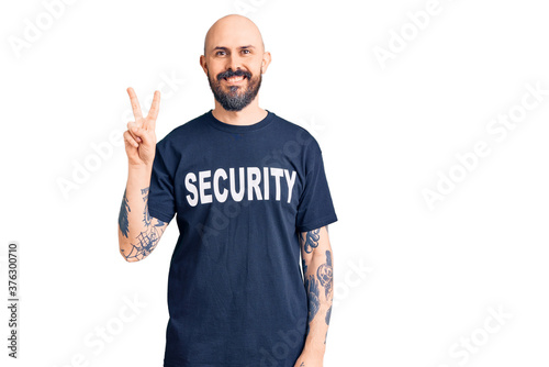 Young handsome man wearing security t shirt smiling looking to the camera showing fingers doing victory sign. number two.