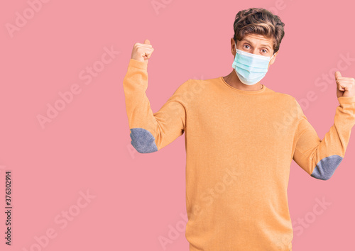 Young handsome man wearing medical mask screaming proud  celebrating victory and success very excited with raised arms