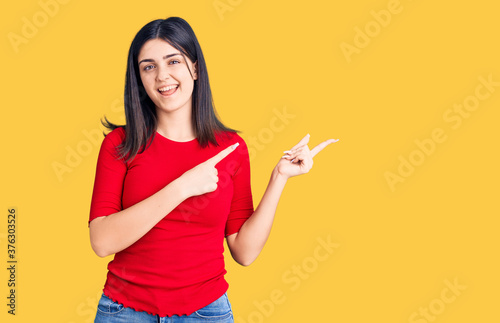 Young beautiful girl wearing casual t shirt smiling and looking at the camera pointing with two hands and fingers to the side.