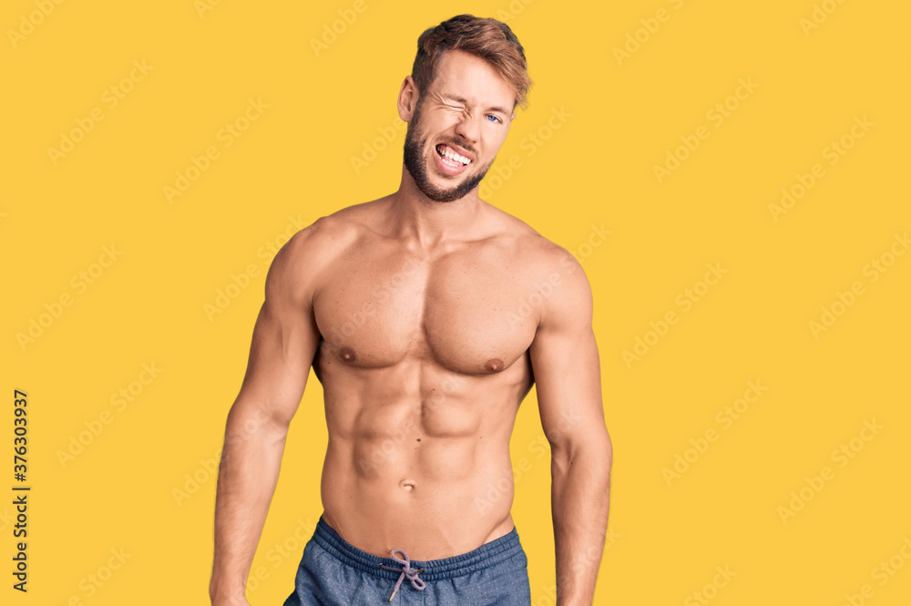 Young caucasian man standing shirtless winking looking at the camera with sexy expression, cheerful and happy face.