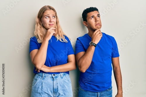 Young interracial couple wearing casual clothes thinking worried about a question, concerned and nervous with hand on chin