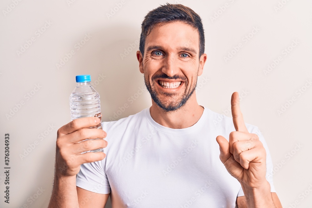 Young handsome man drinking bottle of water to refreshment over isolated white background smiling with an idea or question pointing finger with happy face, number one Young handsome man drinking bottle of water to refreshment over isolated white background smiling with an idea or question pointing finger with happy face, number one