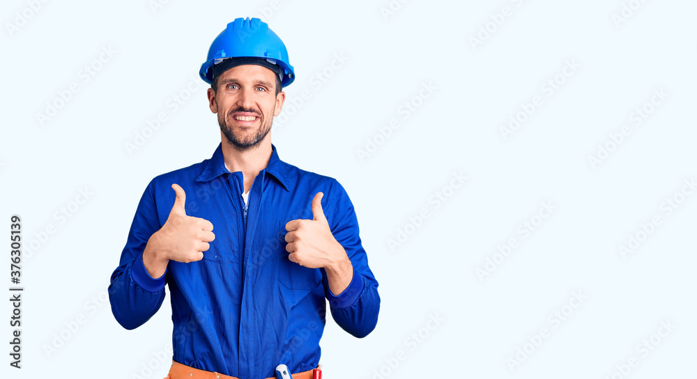Young handsome man wearing worker uniform and hardhat success sign doing positive gesture with hand, thumbs up smiling and happy. cheerful expression and winner gesture. Young handsome man wearing worker uniform and hardhat success sign doing positive gesture with hand, thumbs up smiling and happy. cheerful expression and winner gesture.