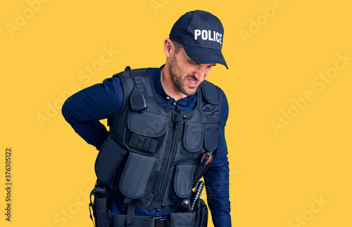 Young handsome man wearing police uniform suffering of backache, touching back with hand, muscular pain