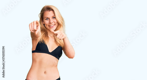 Young beautiful blonde woman wearing bikini pointing to you and the camera with fingers, smiling positive and cheerful