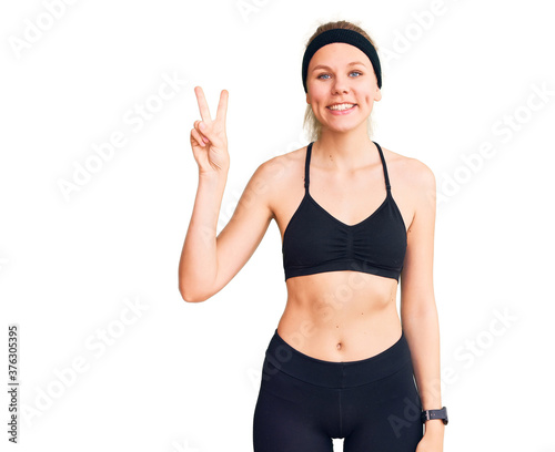 Young beautiful blonde woman wearing sportswear showing and pointing up with fingers number two while smiling confident and happy. © Krakenimages.com