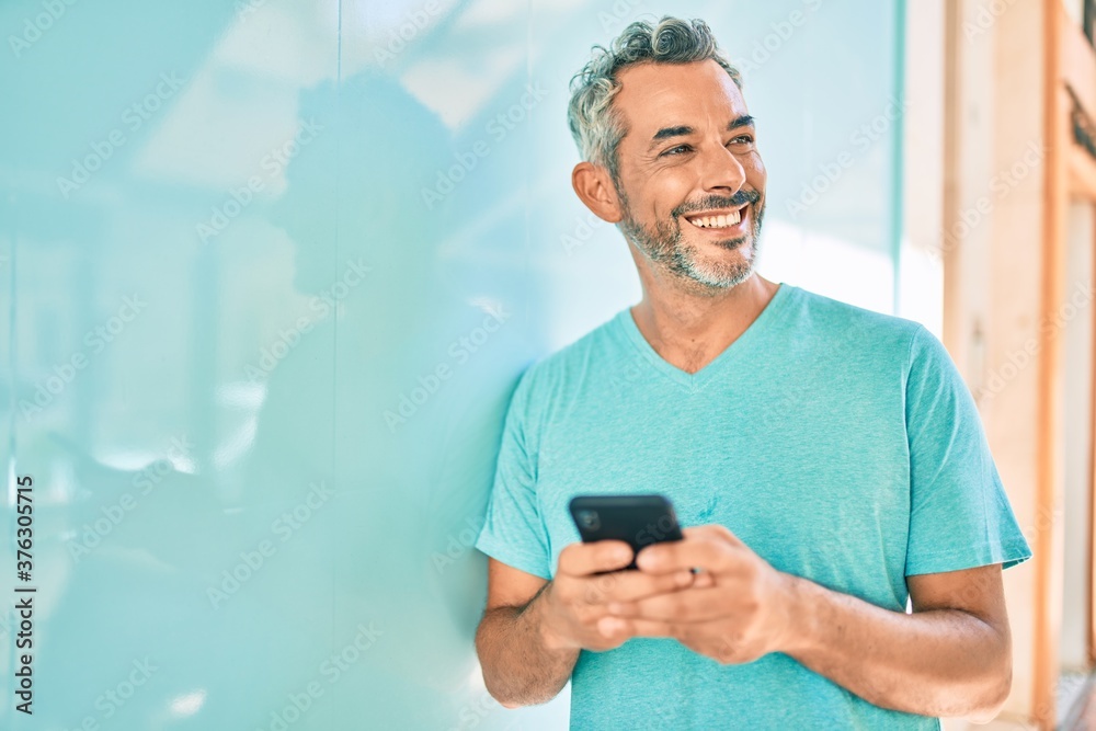 Middle age grey-haired man using smartphone leaning on the wall at city. Middle age grey-haired man using smartphone leaning on the wall at city.