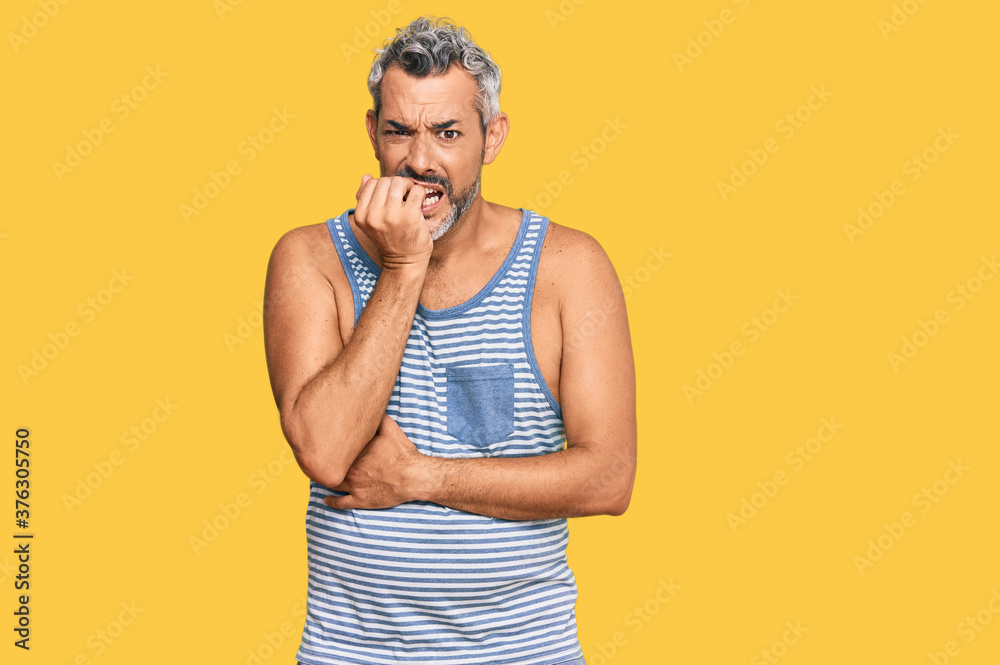 Middle age grey-haired man wearing casual style with sleeveless shirt looking stressed and nervous with hands on mouth biting nails. anxiety problem. Middle age grey-haired man wearing casual style with sleeveless shirt looking stressed and nervous with hands on mouth biting nails. anxiety problem.