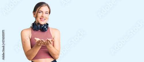 Beautiful caucasian young woman wearing gym clothes and using headphones smiling with hands palms together receiving or giving gesture. hold and protection