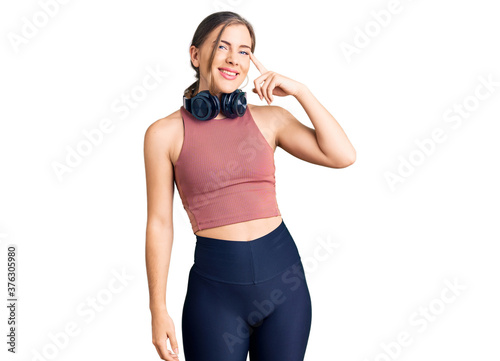 Beautiful caucasian young woman wearing gym clothes and using headphones smiling pointing to head with one finger, great idea or thought, good memory