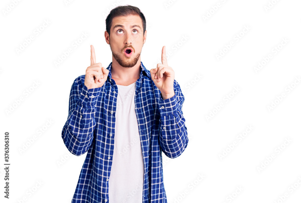 Young handsome caucasian man wearing casual clothes amazed and surprised looking up and pointing with fingers and raised arms. Young handsome caucasian man wearing casual clothes amazed and surprised looking up and pointing with fingers and raised arms.