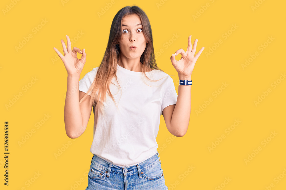 Beautiful caucasian woman wearing casual white tshirt looking surprised and shocked doing ok approval symbol with fingers. crazy expression Beautiful caucasian woman wearing casual white tshirt looking surprised and shocked doing ok approval symbol with fingers. crazy expression