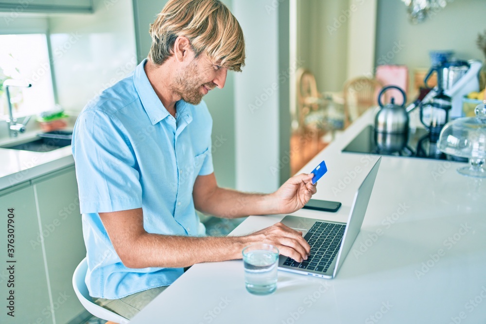 Young irish man using credit card and laptop to buy sitting on the table at home.