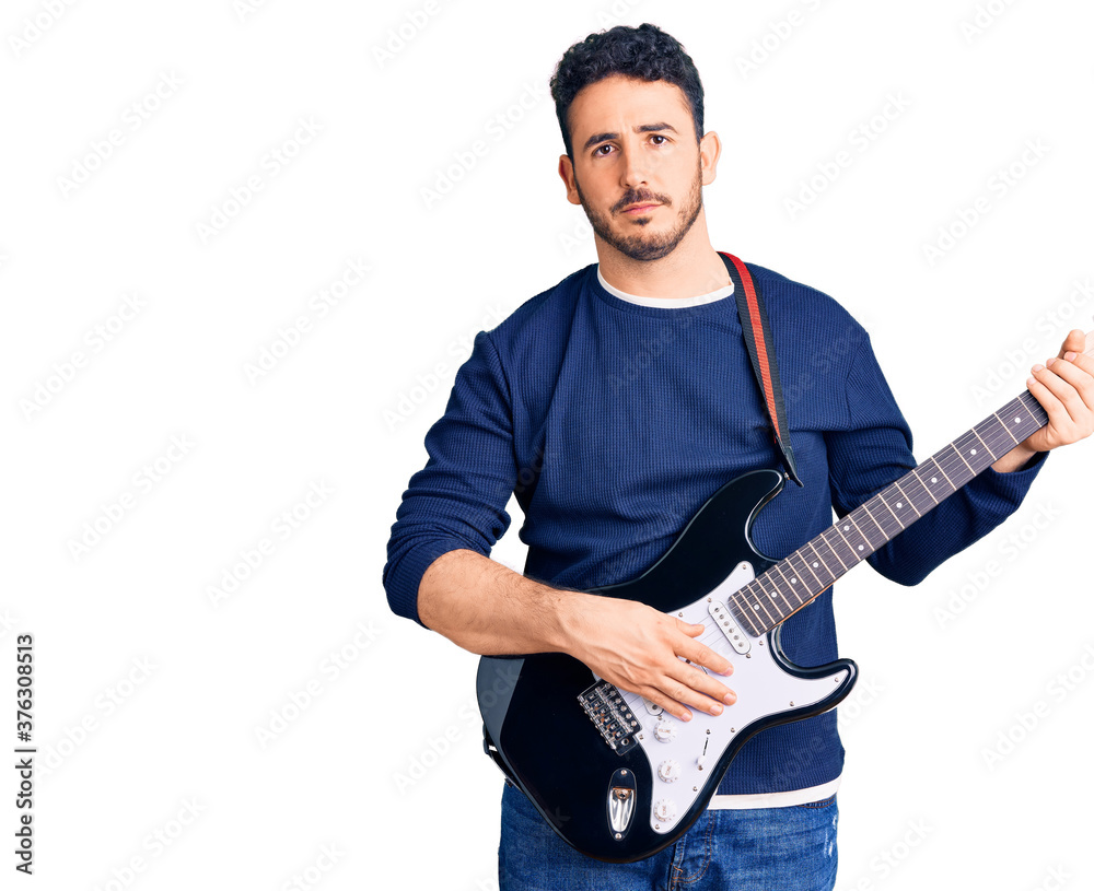Young hispanic man playing electric guitar thinking attitude and sober expression looking self confident Young hispanic man playing electric guitar thinking attitude and sober expression looking self confident