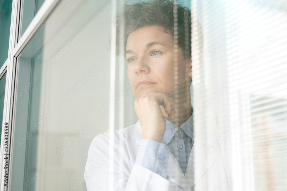 Young pensive female scientist or researcher in whitecoat keeping hand by chin Young pensive female scientist or researcher in whitecoat keeping hand by chin