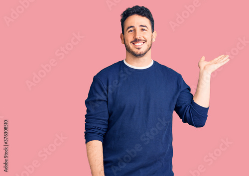 Young hispanic man wearing casual clothes smiling cheerful presenting and pointing with palm of hand looking at the camera.