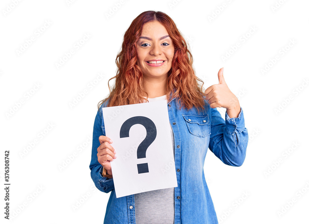Young latin woman holding question mark smiling happy and positive, thumb up doing excellent and approval sign Young latin woman holding question mark smiling happy and positive, thumb up doing excellent and approval sign