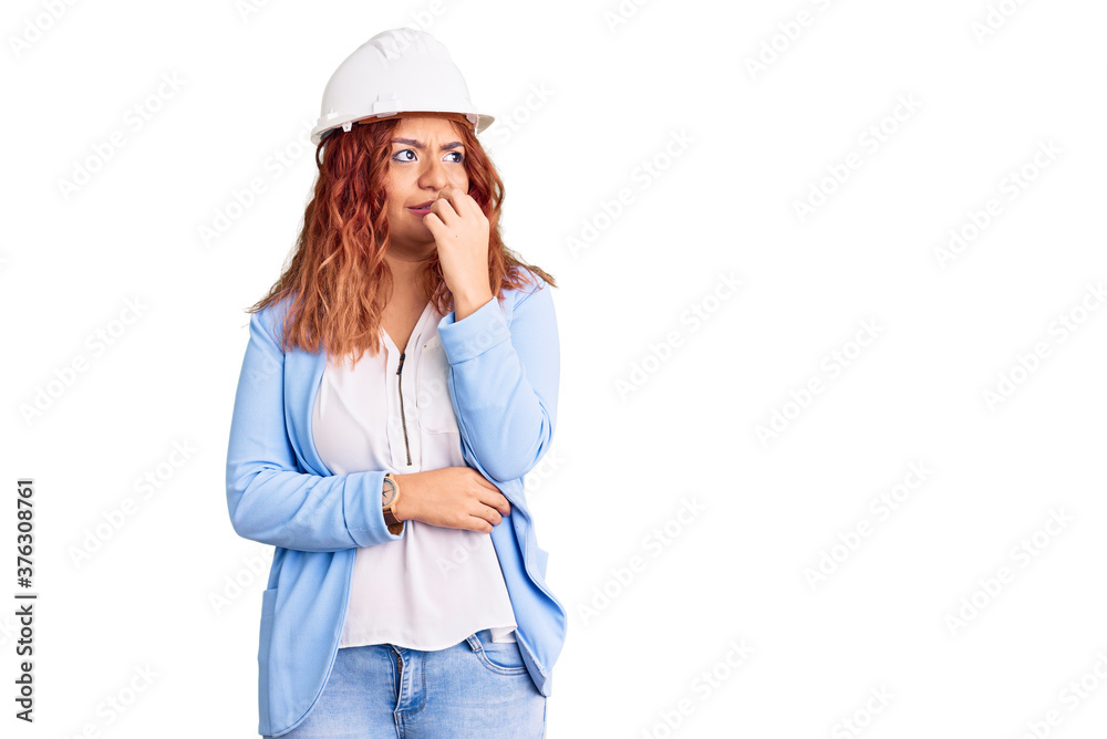Young latin woman wearing architect hardhat looking stressed and nervous with hands on mouth biting nails. anxiety problem.
