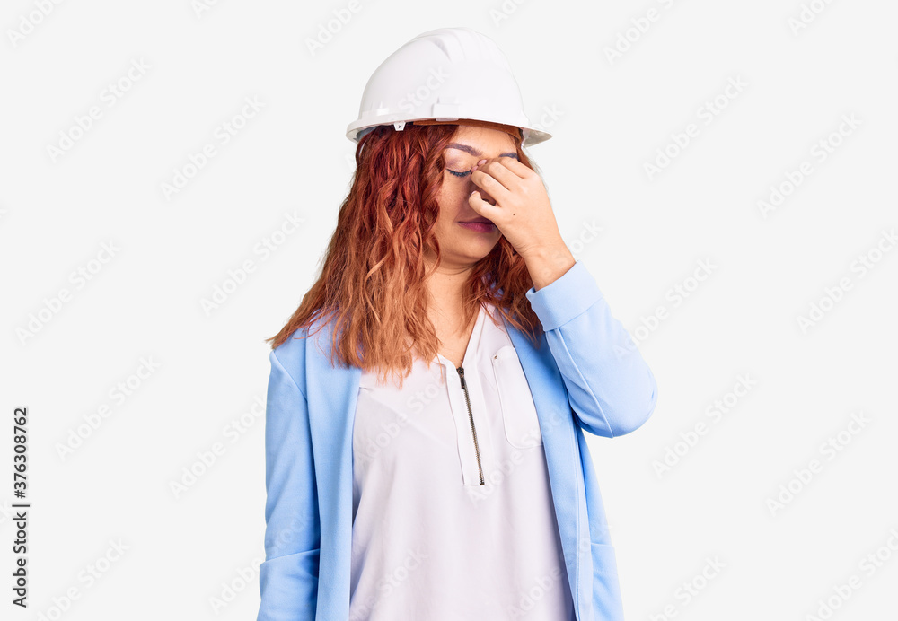 Young latin woman wearing architect hardhat tired rubbing nose and eyes feeling fatigue and headache. stress and frustration concept. Young latin woman wearing architect hardhat tired rubbing nose and eyes feeling fatigue and headache. stress and frustration concept.