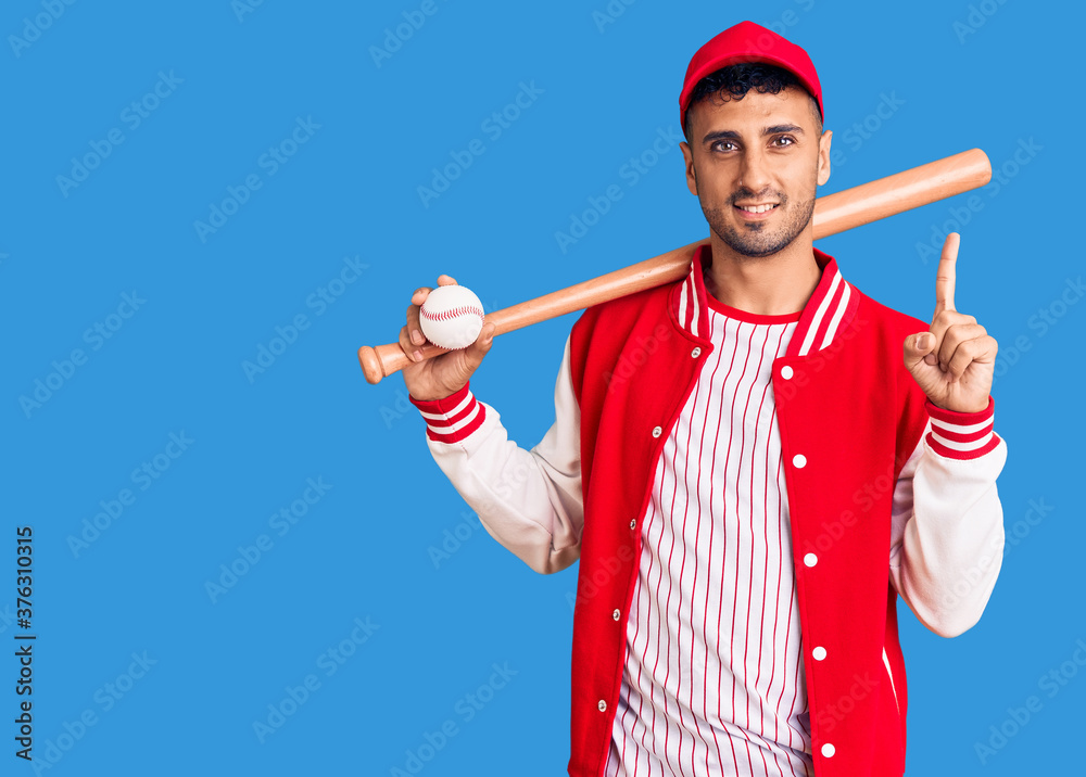 Young hispanic man playing baseball holding bat and ball surprised with an idea or question pointing finger with happy face, number one Young hispanic man playing baseball holding bat and ball surprised with an idea or question pointing finger with happy face, number one