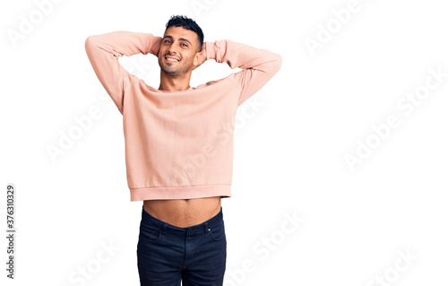 Young hispanic man wearing casual clothes relaxing and stretching, arms and hands behind head and neck smiling happy photo