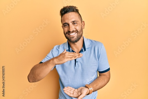 Handsome man with beard wearing casual clothes gesturing with hands showing big and large size sign, measure symbol. smiling looking at the camera. measuring concept.