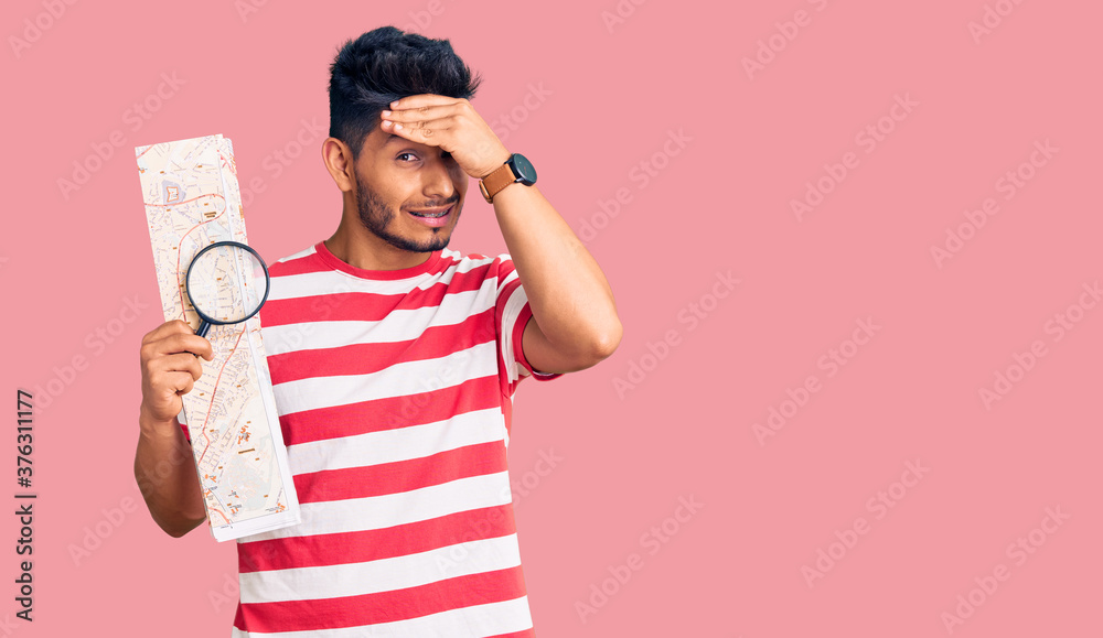 Handsome latin american young man looking at city map with magnifying glass stressed and frustrated with hand on head, surprised and angry face Handsome latin american young man looking at city map with magnifying glass stressed and frustrated with hand on head, surprised and angry face