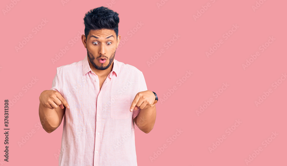 Handsome latin american young man wearing casual summer shirt pointing down with fingers showing advertisement, surprised face and open mouth Handsome latin american young man wearing casual summer shirt pointing down with fingers showing advertisement, surprised face and open mouth