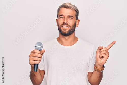 Handsome blond singer man with beard singing song using microphone over white background smiling happy pointing with hand and finger to the side