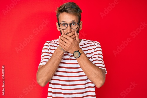 Handsome caucasian man with beard wearing casual clothes and glasses shocked covering mouth with hands for mistake. secret concept.