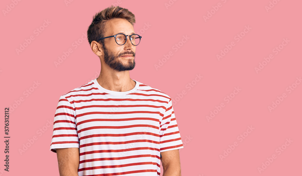 Handsome blond man with beard wearing casual clothes and glasses smiling looking to the side and staring away thinking. Handsome blond man with beard wearing casual clothes and glasses smiling looking to the side and staring away thinking.