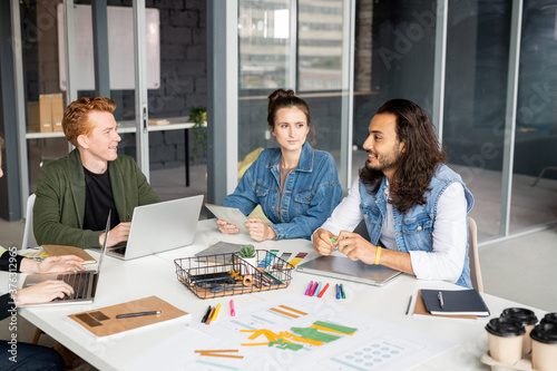 Group of young contemporary developers of mobile applications gathered by table