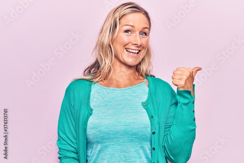 Middle age caucasian blonde woman wearing casual clothes pointing thumb up to the side smiling happy with open mouth