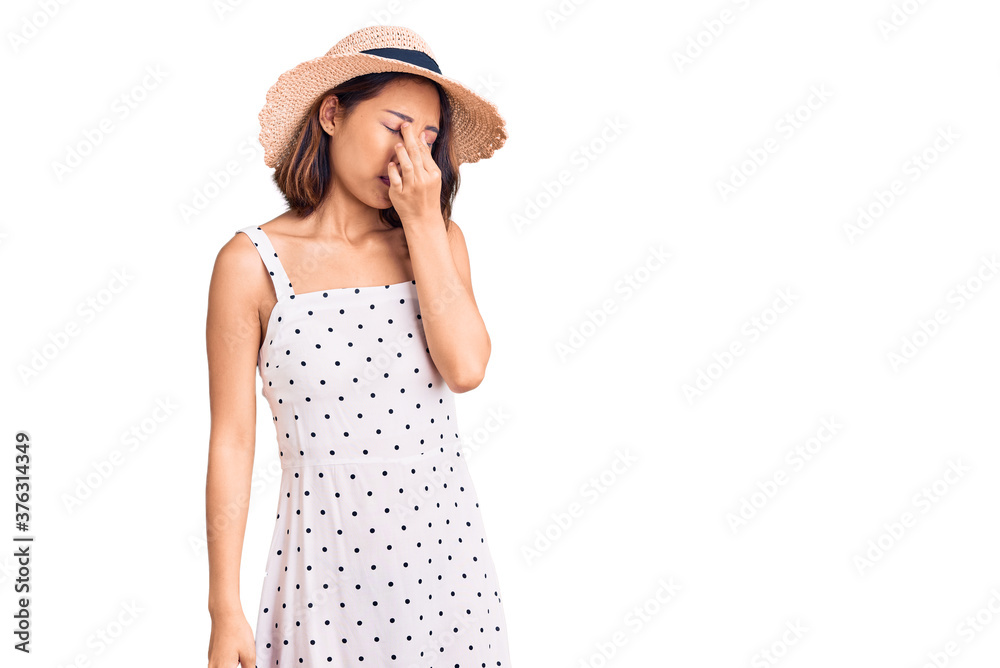 Young beautiful chinese girl wearing summer hat tired rubbing nose and eyes feeling fatigue and headache. stress and frustration concept. Young beautiful chinese girl wearing summer hat tired rubbing nose and eyes feeling fatigue and headache. stress and frustration concept.