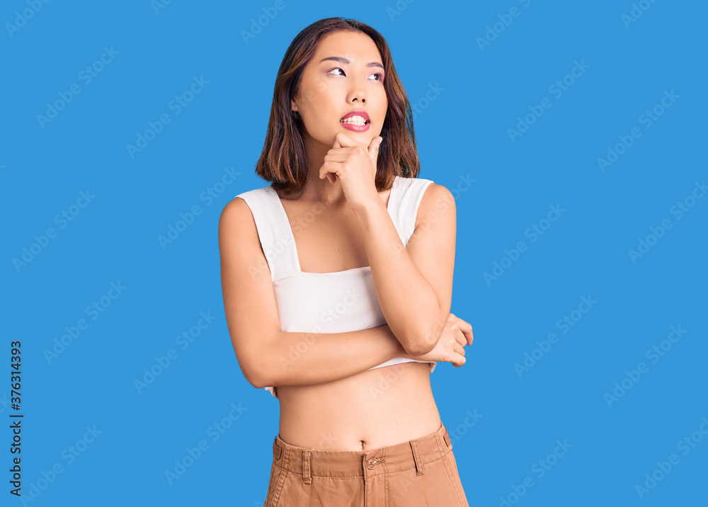 Fototapeta premium Young beautiful chinese girl wearing casual clothes with hand on chin thinking about question, pensive expression. smiling with thoughtful face. doubt concept.