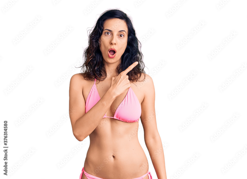 Fototapeta premium Young beautiful hispanic woman wearing bikini surprised pointing with finger to the side, open mouth amazed expression.