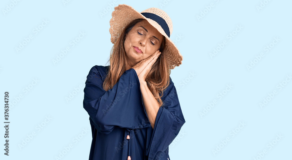 Fototapeta premium Middle age hispanic woman wearing summer hat sleeping tired dreaming and posing with hands together while smiling with closed eyes.