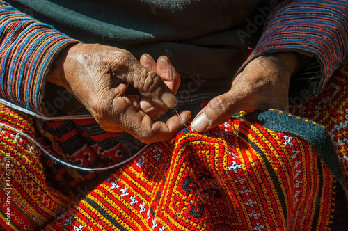 Tableau sur toile Hands of a Black Hmong woman sewing colorful traditional fabric and other arts and crafts with her hands in the sunlight, North Vietnam