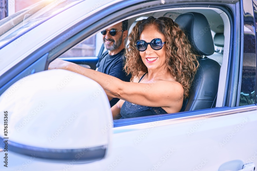 Middle age beautiful couple on vacation wearing sunglasses smiling happy driving car.