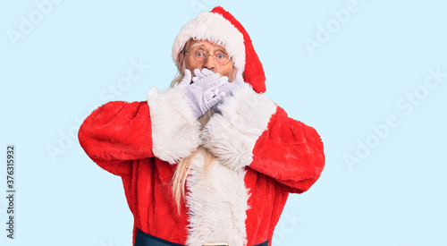 Old senior man with grey hair and long beard wearing traditional santa claus costume shocked covering mouth with hands for mistake. secret concept.