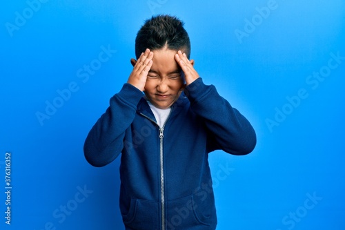 Little boy hispanic kid wearing casual sporty jacket with hand on head, headache because stress. suffering migraine.