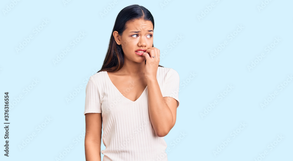 Young beautiful latin girl wearing casual white t shirt looking stressed and nervous with hands on mouth biting nails. anxiety problem. Young beautiful latin girl wearing casual white t shirt looking stressed and nervous with hands on mouth biting nails. anxiety problem.