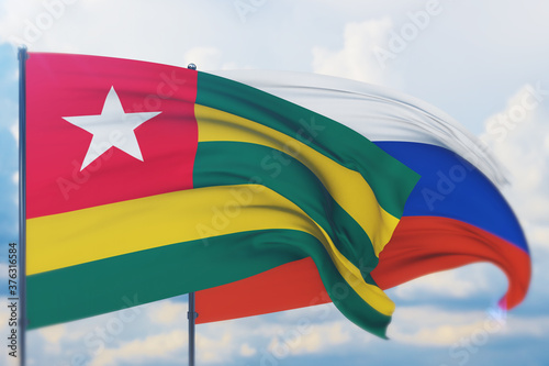 Waving Russian flag and flag of Togo. Closeup view, 3D illustration.
