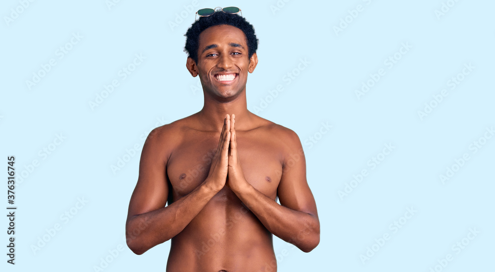 African handsome man wearing swimsuit and sunglasses praying with hands together asking for forgiveness smiling confident.