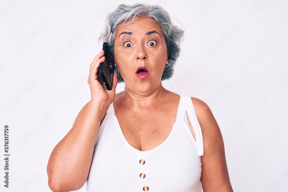 Naklejka premium Senior hispanic grey- haired woman having conversation talking on the smartphone scared and amazed with open mouth for surprise, disbelief face