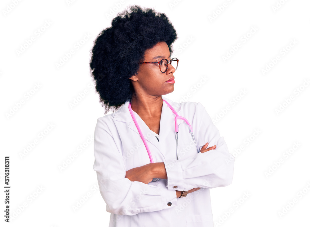 Young african american woman wearing doctor coat and stethoscope looking to the side with arms crossed convinced and confident