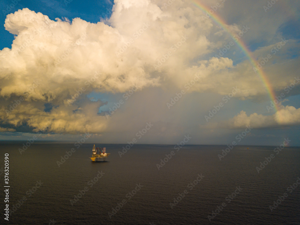 Aerial view from a drone of an offshore jack up rig at the offshore location during raining time with rainbow Aerial view from a drone of an offshore jack up rig at the offshore location during raining time with rainbow